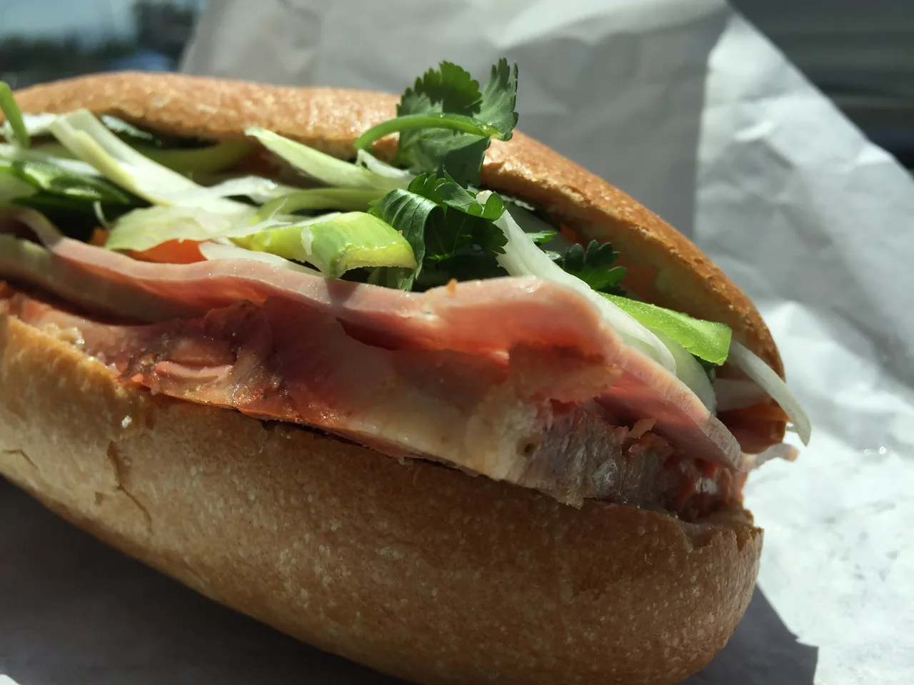 A loaded Vietnamese bánh mì close-up with cold cuts, herbs and pickled vegetables