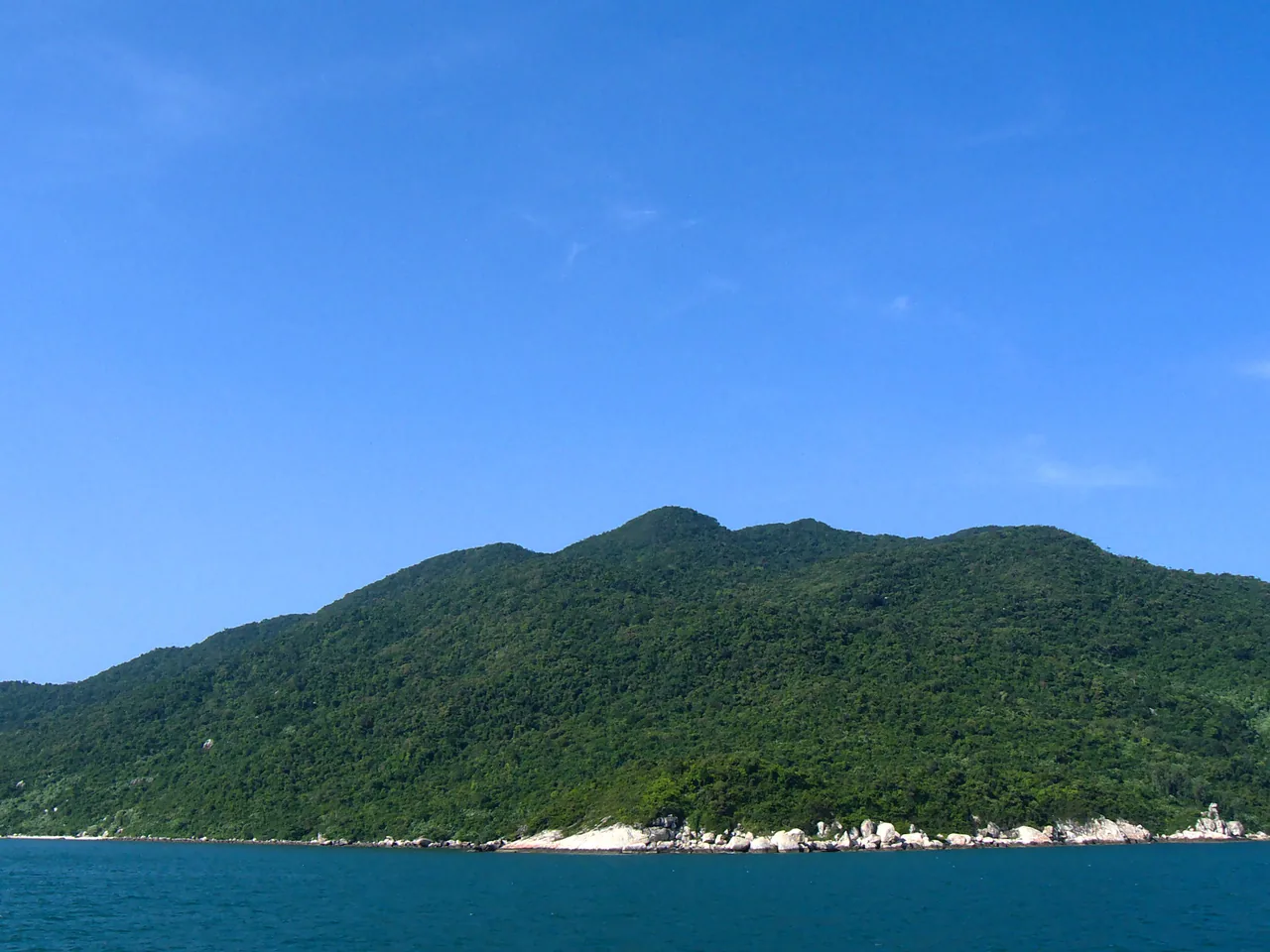A green forested Cham island rising steeply from clear teal sea