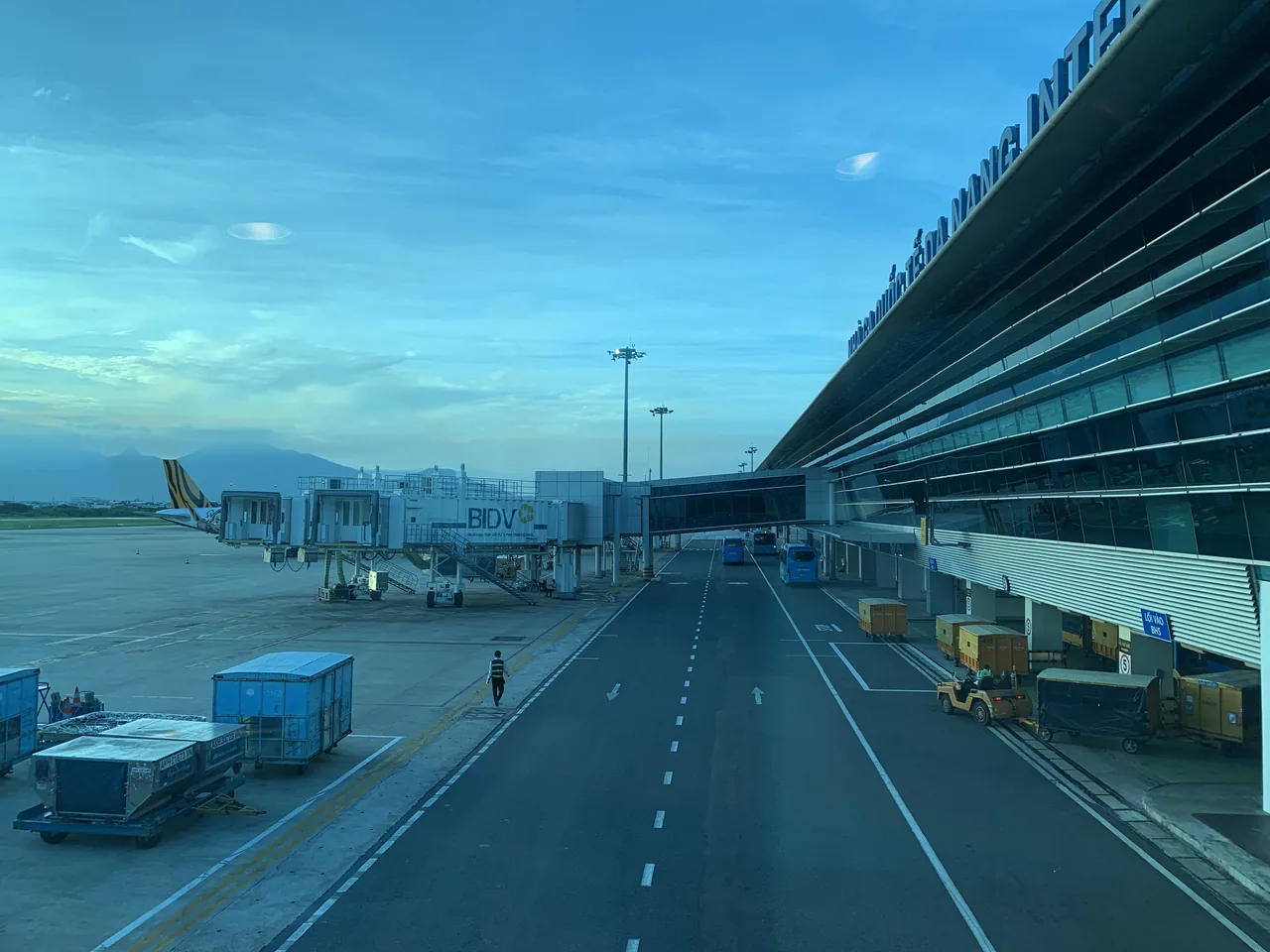 The exterior of Da Nang International Airport terminal, with jet bridges, parked aircraft and mountains behind