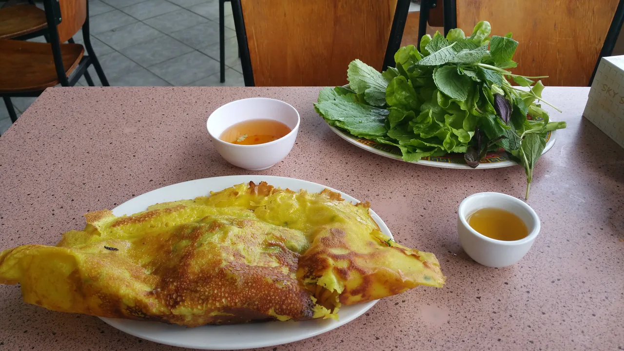 A plate of crispy banh xeo with fresh herbs and dipping sauce