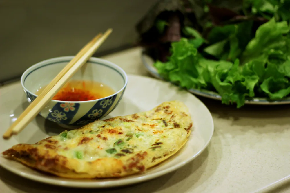 Bánh xèo served with its dipping sauce and a plate of fresh herbs