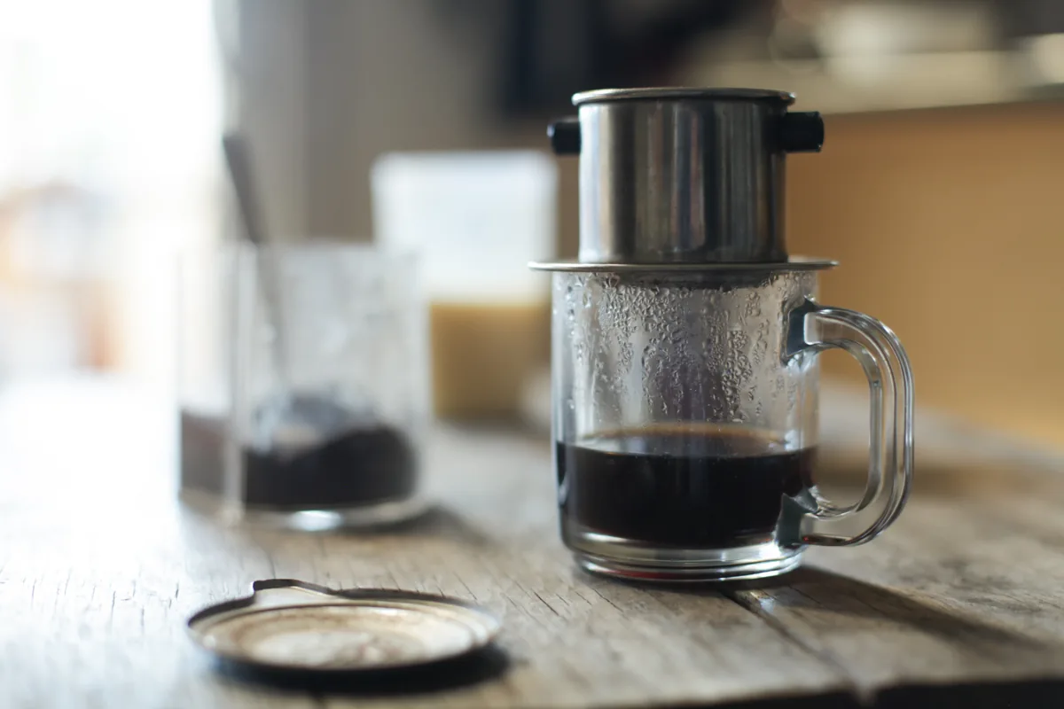 A Vietnamese phin metal filter brewing coffee over a glass