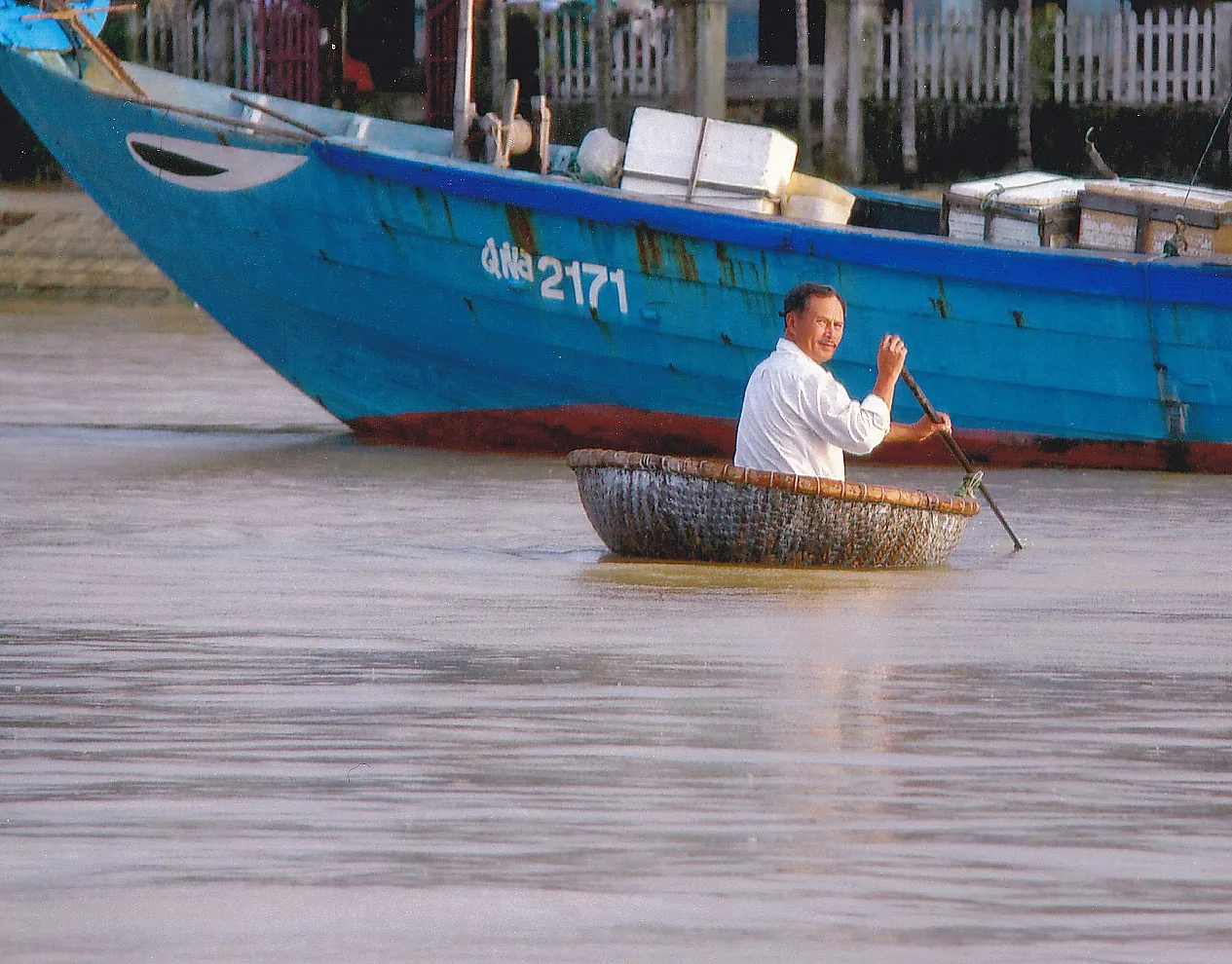 A boatman paddling a round bamboo basket boat with a single oar on the water in central Vietnam