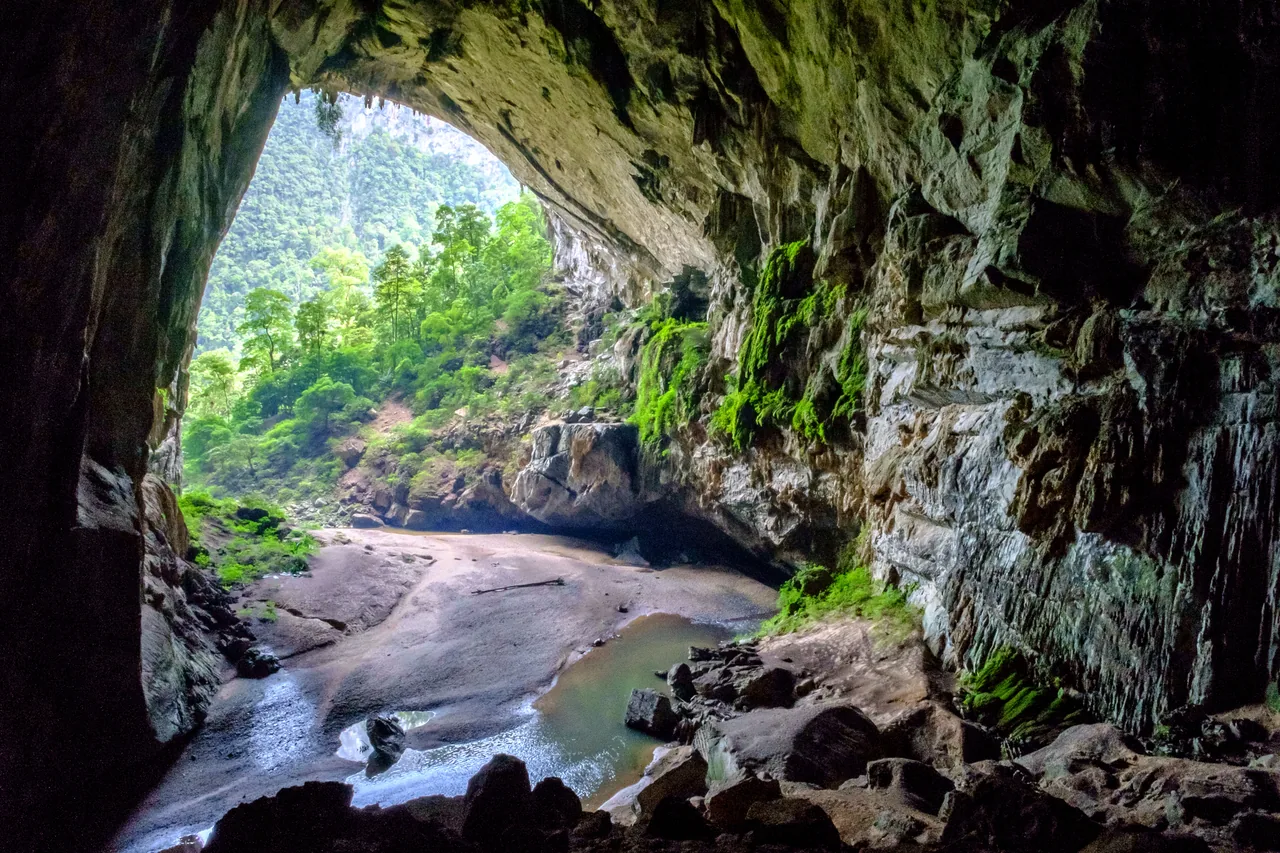 The vast mouth of Hang En, the world's third-largest cave, with a beach and river under a jungle-framed opening