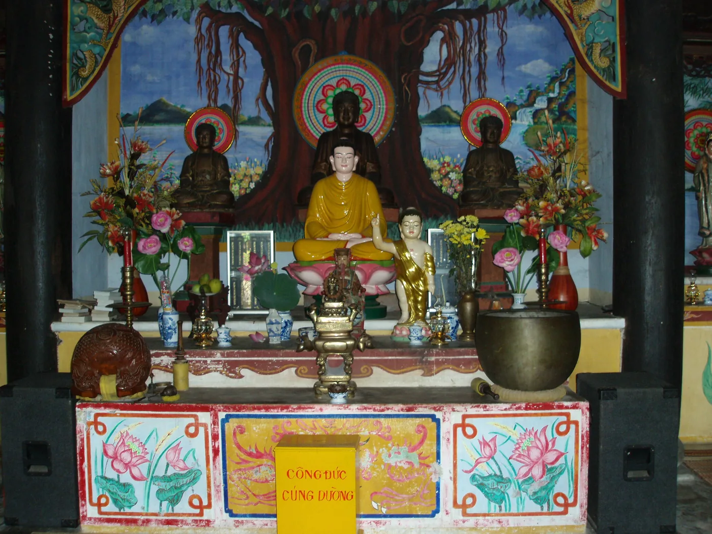 The main altar inside Chùa Hải Tạng, with three seated bronze Buddhas below a painted bodhi tree mural