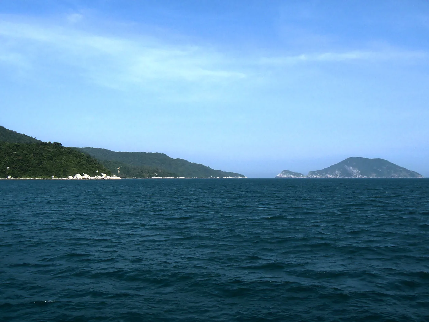 The wooded shore of Cù Lao Chàm with white boulders at the waterline and a separate outer islet to the right