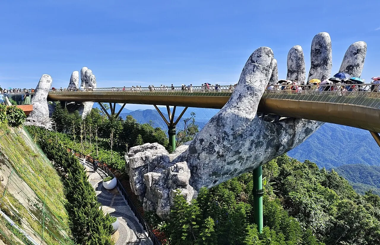 The Golden Bridge at Ba Na Hills held up by two giant stone hands, with a crowd of visitors walking along it The Golden Bridge at Ba Na Hills held up by two giant stone hands, with a crowd of visitors walking along it