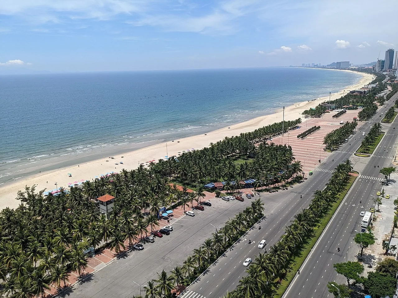 Aerial view over My Khe beach in Da Nang, with a belt of palms, the beach road and high-rise towers behind the sand Aerial view over My Khe beach in Da Nang, with a belt of palms, the beach road and high-rise towers behind the sand