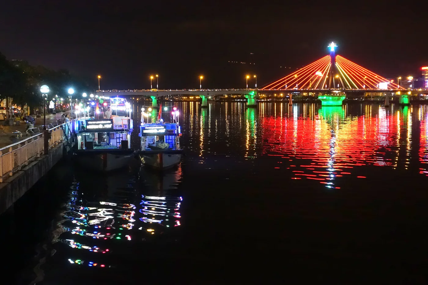 Two lit tourist boats moored at the quay on the Han River at night, with the Han River Bridge lit red, green and yellow behind them