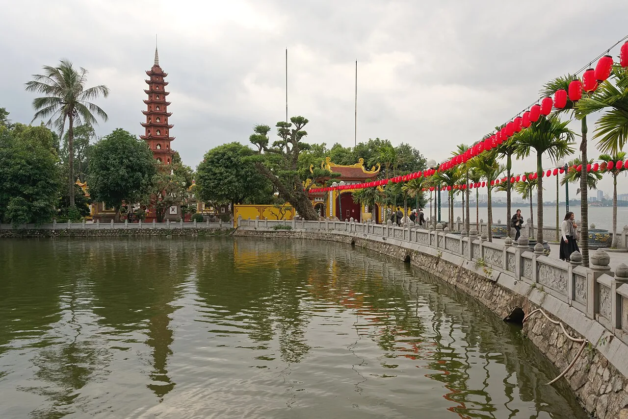 沿著石欄杆堤道望向西湖中小島上的鎮國寺,層層堆疊的紅磚塔與黃色門樓,棕櫚樹上方掛著紅燈籠,右側是開闊的湖面 沿著石欄杆堤道望向西湖中小島上的鎮國寺,層層堆疊的紅磚塔與黃色門樓,棕櫚樹上方掛著紅燈籠,右側是開闊的湖面