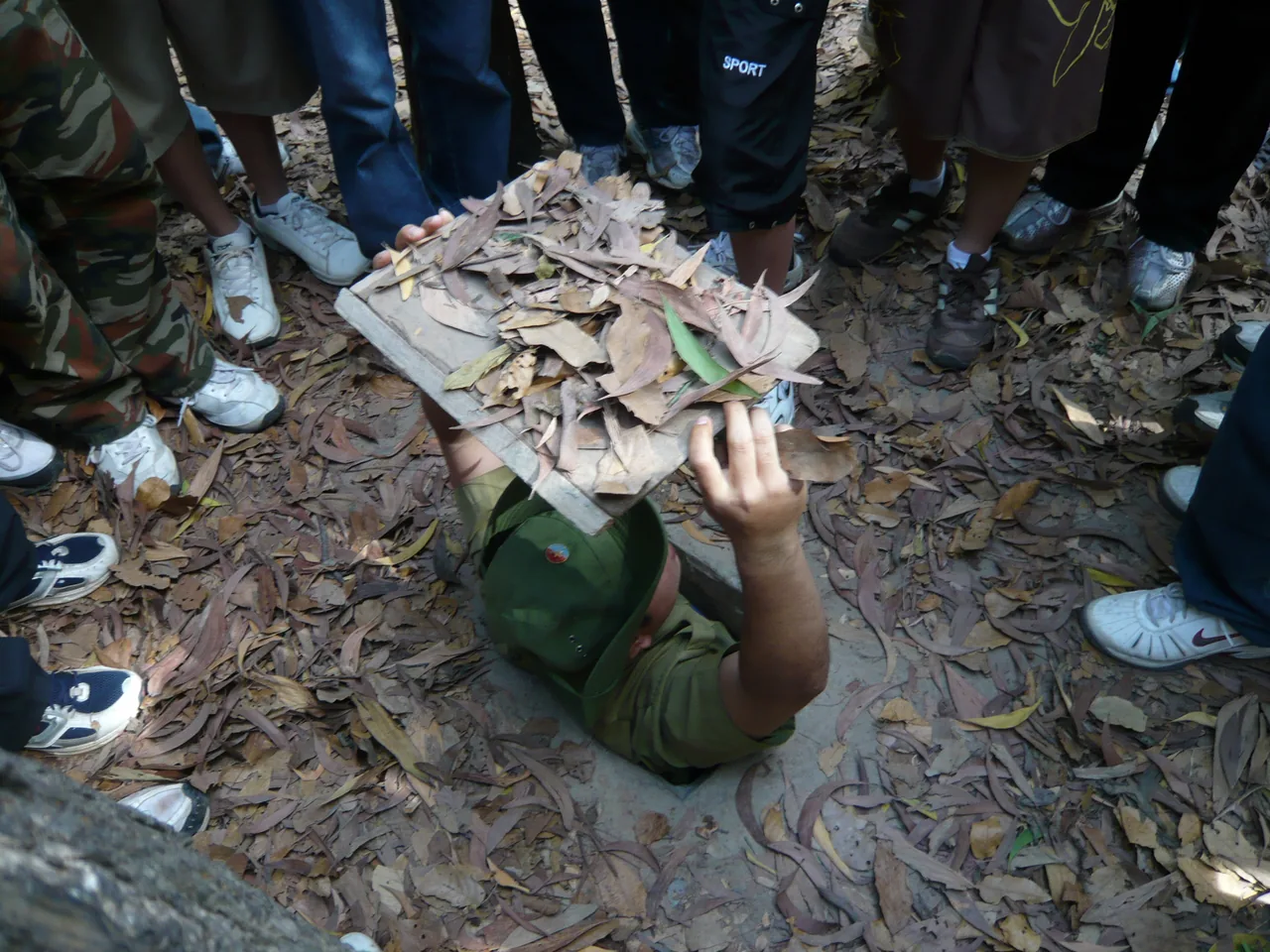 A narrow camouflaged entrance to the Cu Chi Tunnels with a guide demonstrating how fighters disappeared underground.