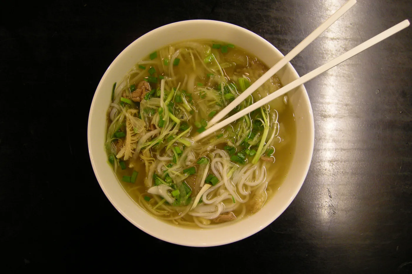 A steaming bowl of phở with rare beef, fresh herbs, lime and chili on a street-side table.