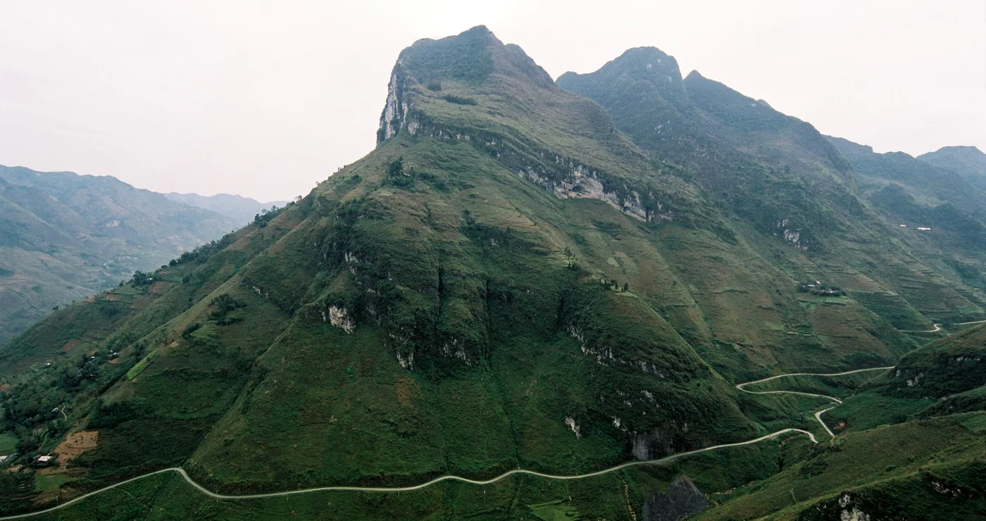 A winding mountain road hugging the cliffs of the Ma Pi Leng Pass on the Ha Giang Loop, deep river gorge below.