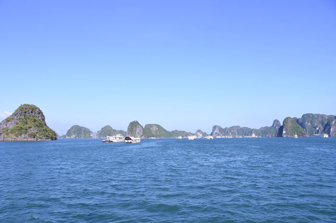 Limestone karst towers rising straight out of the emerald water of Ha Long Bay in northern Vietnam, with a wooden cruise junk in the foreground.