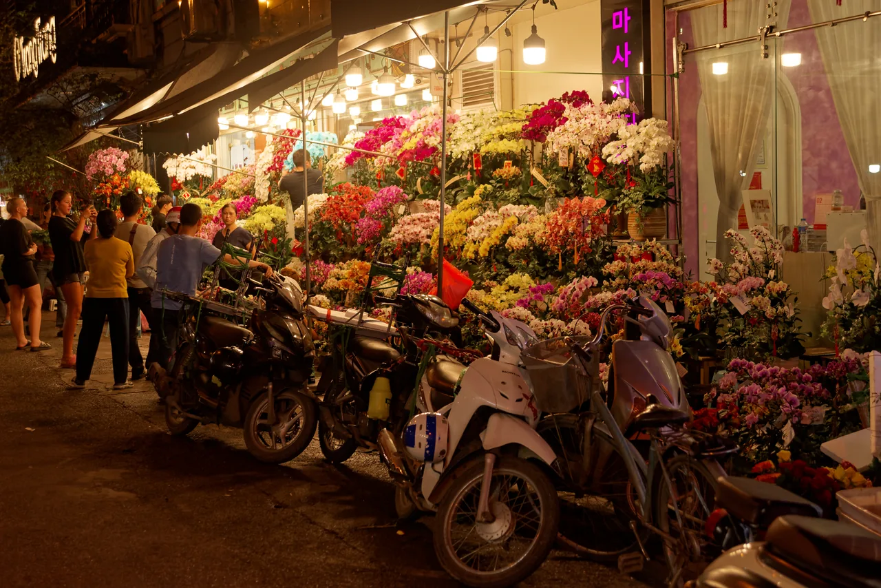 A motorbike-filled street in Hanoi's Old Quarter with colonial-era shophouses and hanging shop signs.