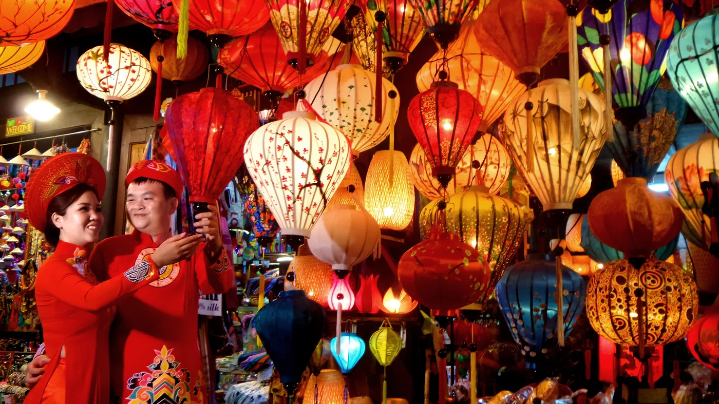 Silk lanterns glowing over the Thu Bon riverfront in Hoi An's old town at dusk, boats drifting past.