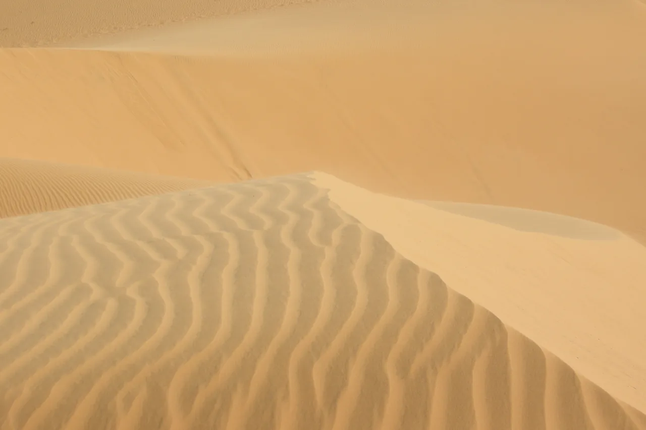 Rippling orange sand dunes at Mui Ne under a bright sky, a lone figure walking the crest.