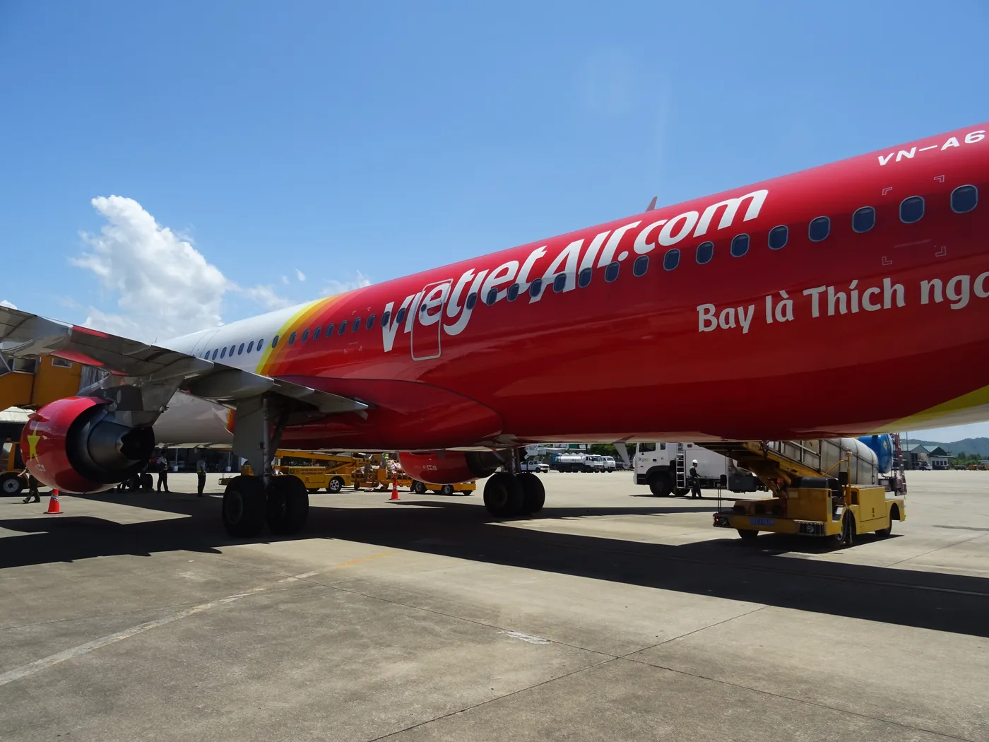 A domestic airliner on the apron at a Vietnamese airport with ground crew loading baggage