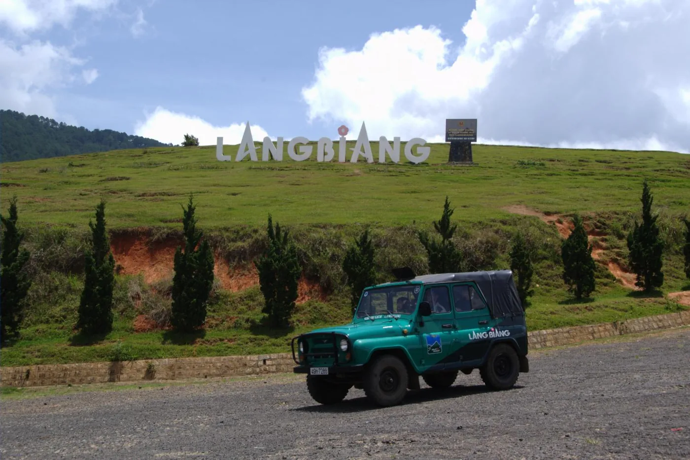 The LANGBIANG sign on a grass slope with a green jeep parked on the road below
