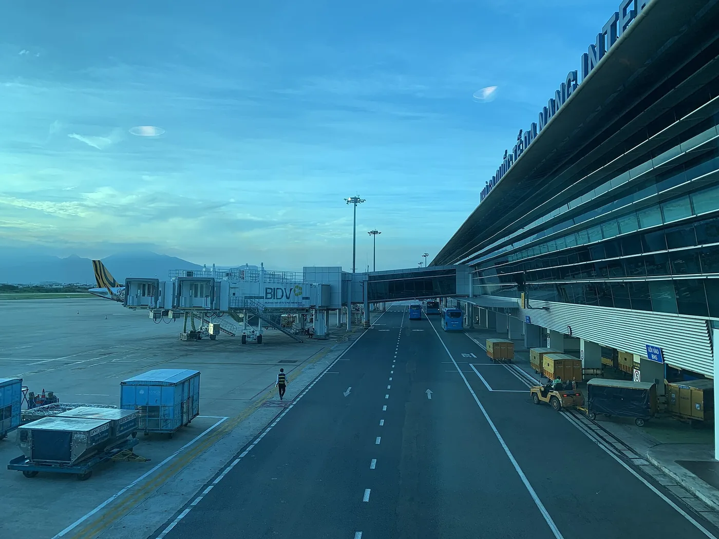 The frontage of the international terminal at Da Nang airport at dusk with airbridges along it and buses waiting