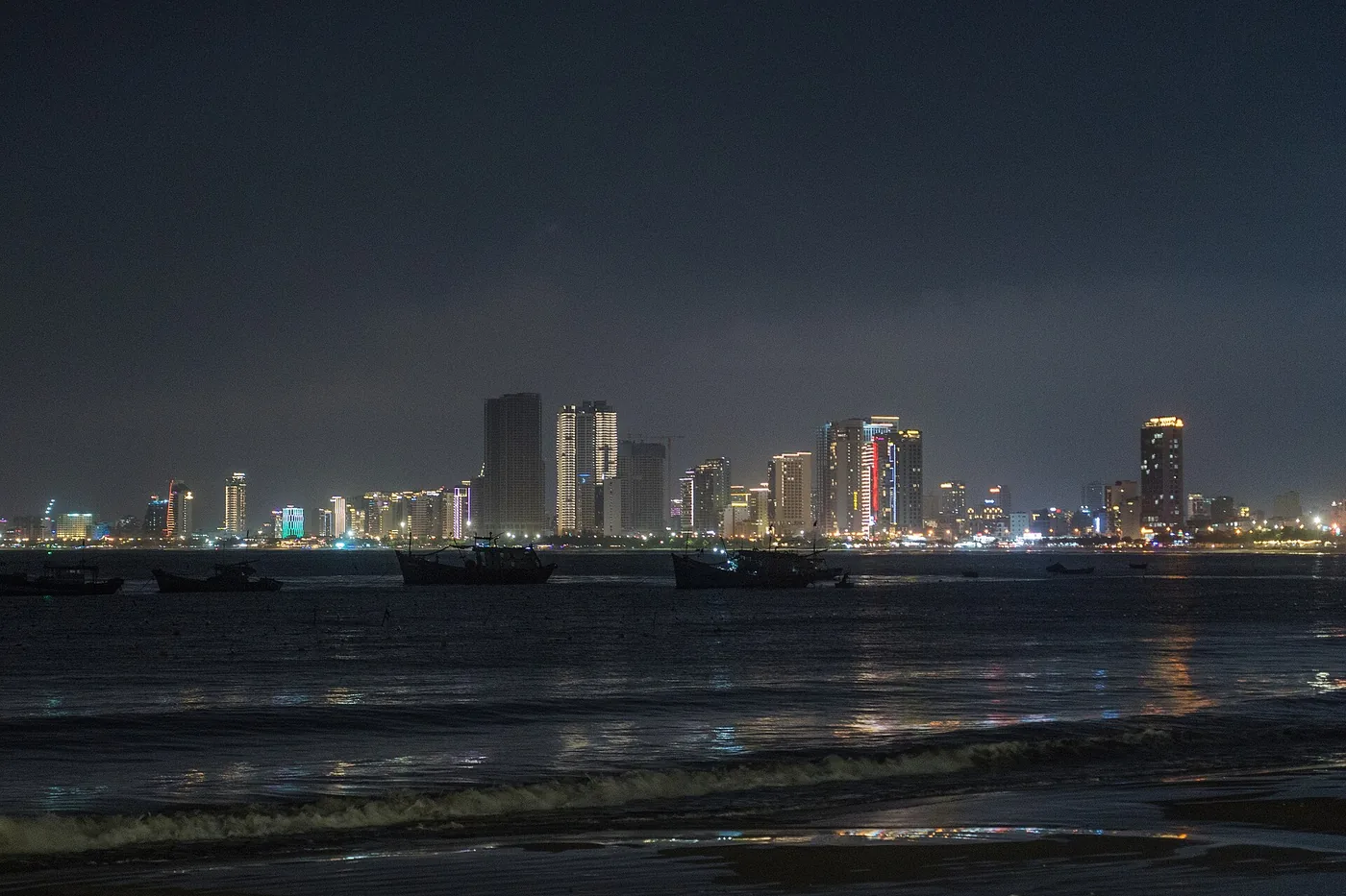 The Da Nang skyline lit up at night across the water with fishing boats moored in the foreground