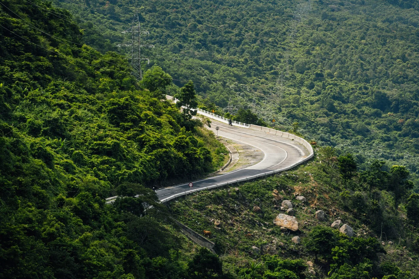 A hairpin bend on the Hai Van Pass seen from above, the road doubling back across a green hillside