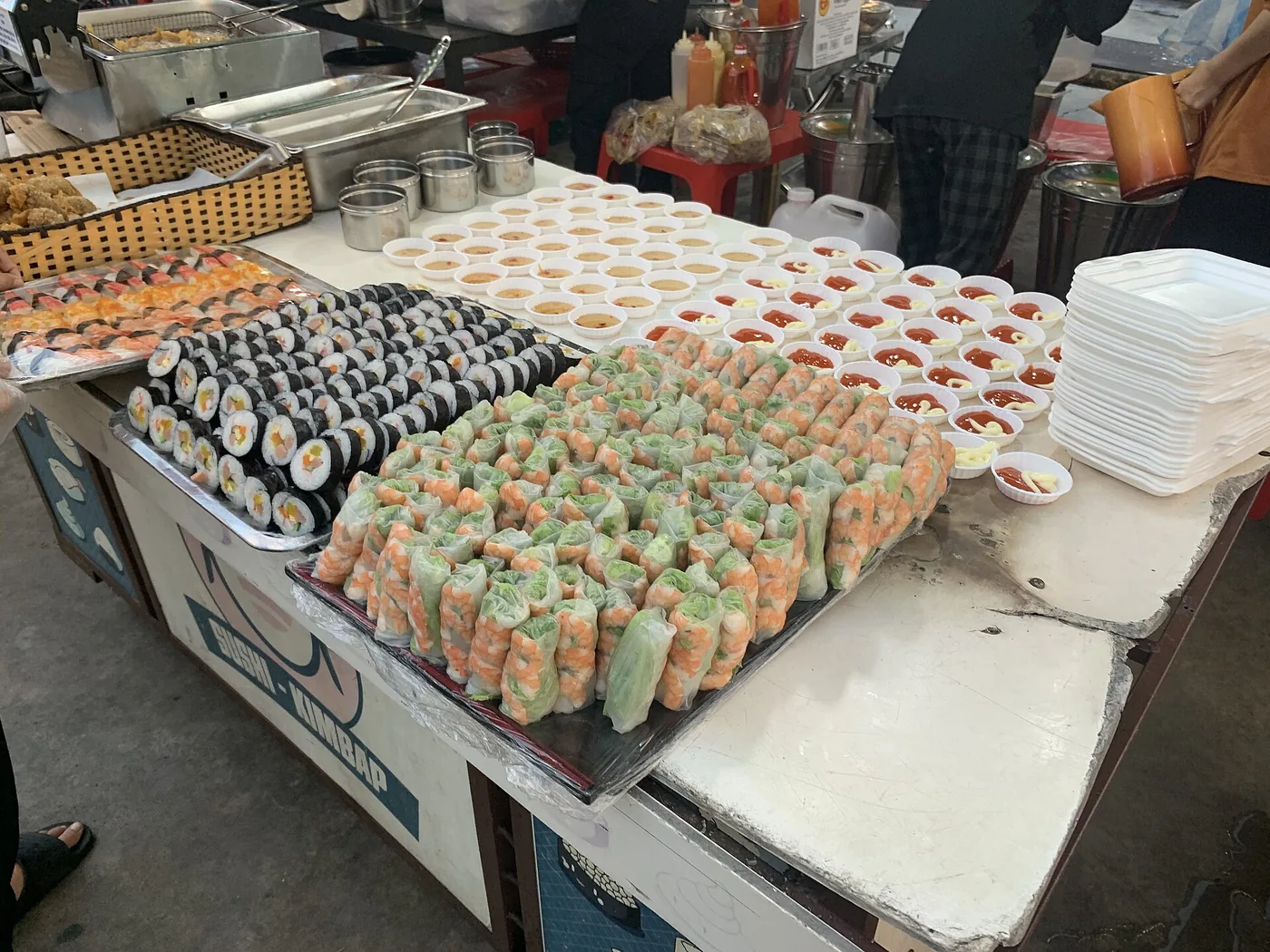A stall at the Helio night market in Da Nang with trays of rice paper rolls and seaweed rolls and rows of small sauce bowls