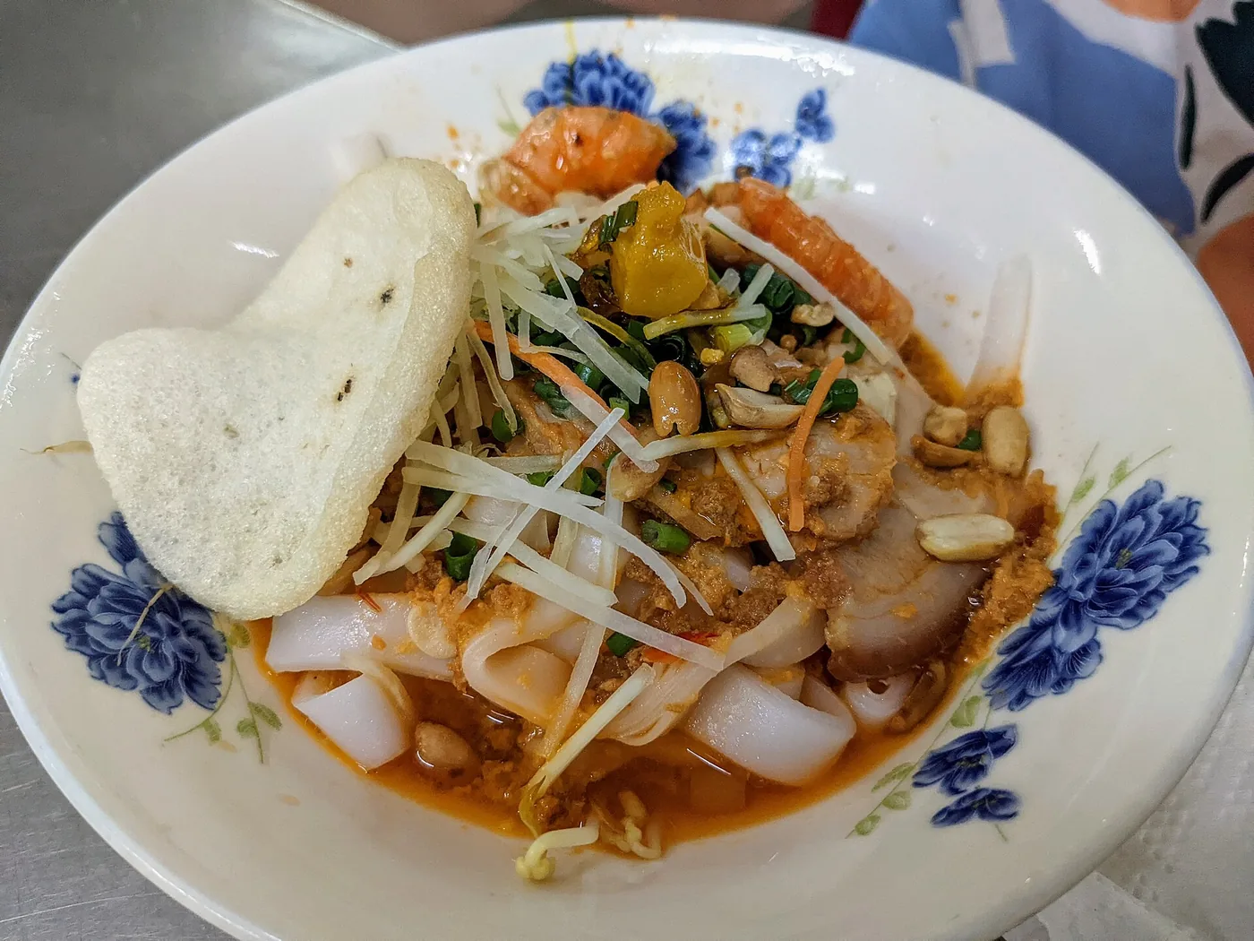 A single bowl of mi quang at Mi Quang 1A in Da Nang with flat noodles, pork, a prawn, peanuts, herbs and a sesame rice cracker