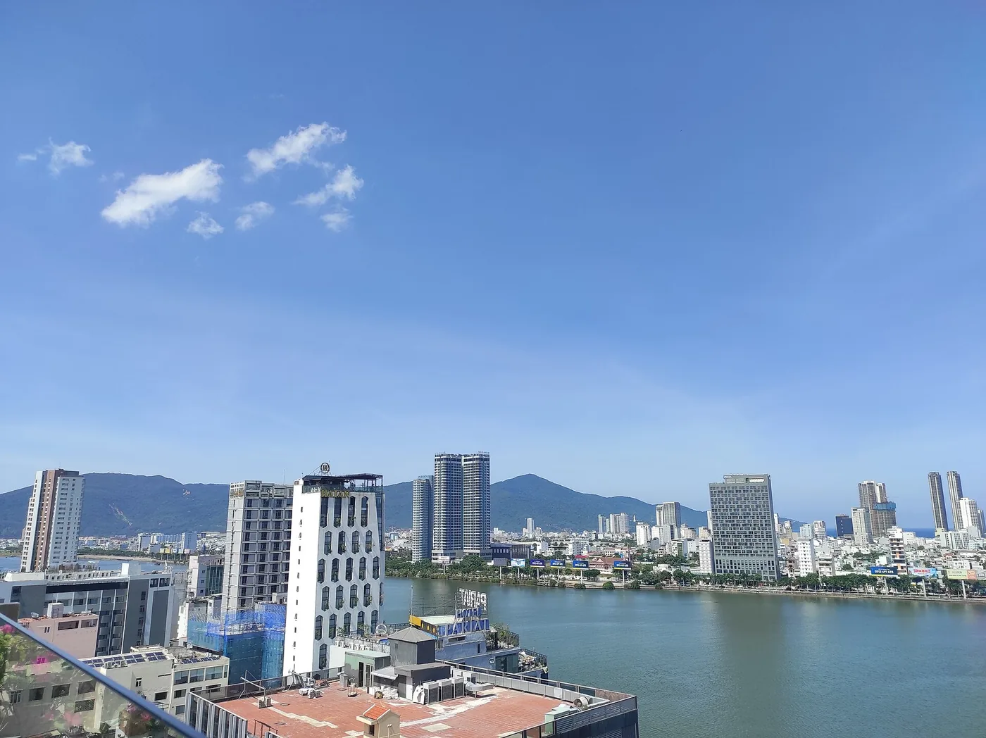 Both banks of the Han River in Da Nang from above, towers lining the water and the Son Tra hills behind