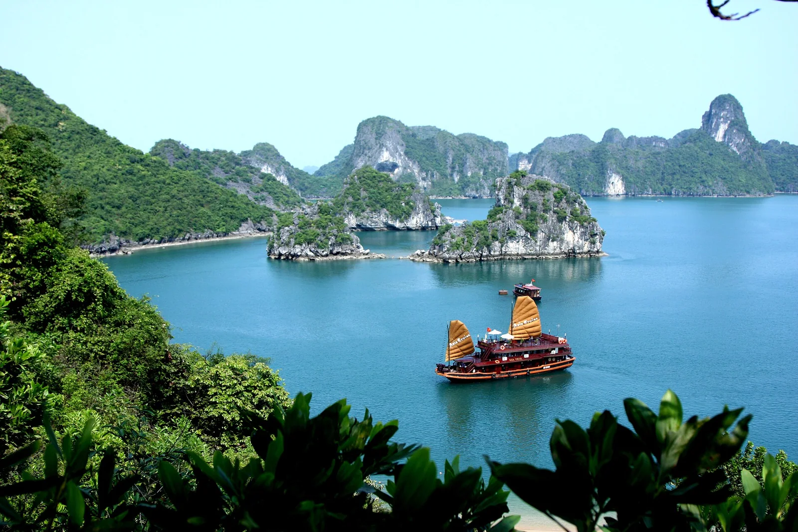 A wooden junk with dark sails cruising between limestone karst islands on Ha Long Bay