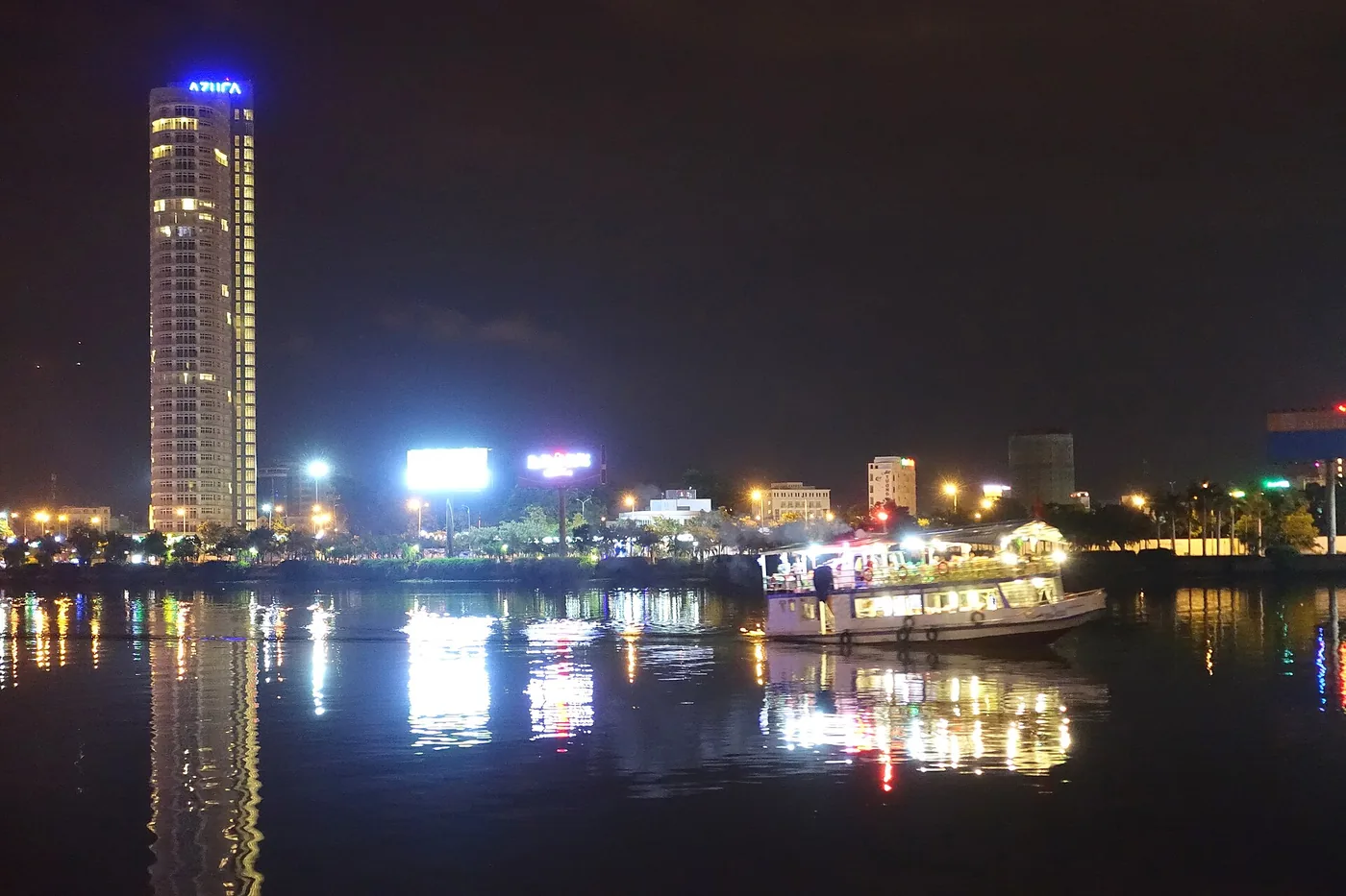 A lit tourist boat on the Han River in Da Nang at night, with the city lights reflected in the water