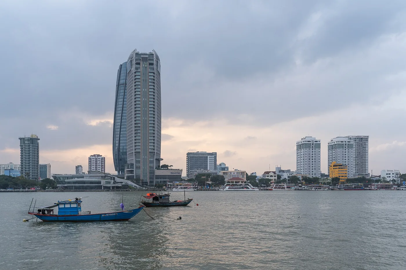 White tourist cruise boats moored on the Bach Dang riverfront in Da Nang, with the curved Novotel tower behind