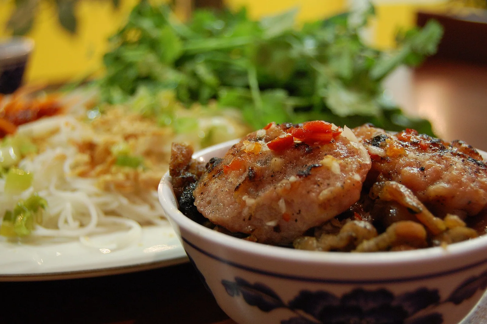 A bowl of bun cha with charcoal-grilled pork patties sitting in dipping sauce beside cold rice noodles