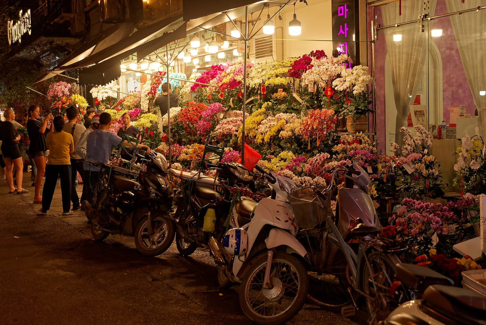 A lit flower shop and parked scooters on a narrow street in the Hanoi Old Quarter at night