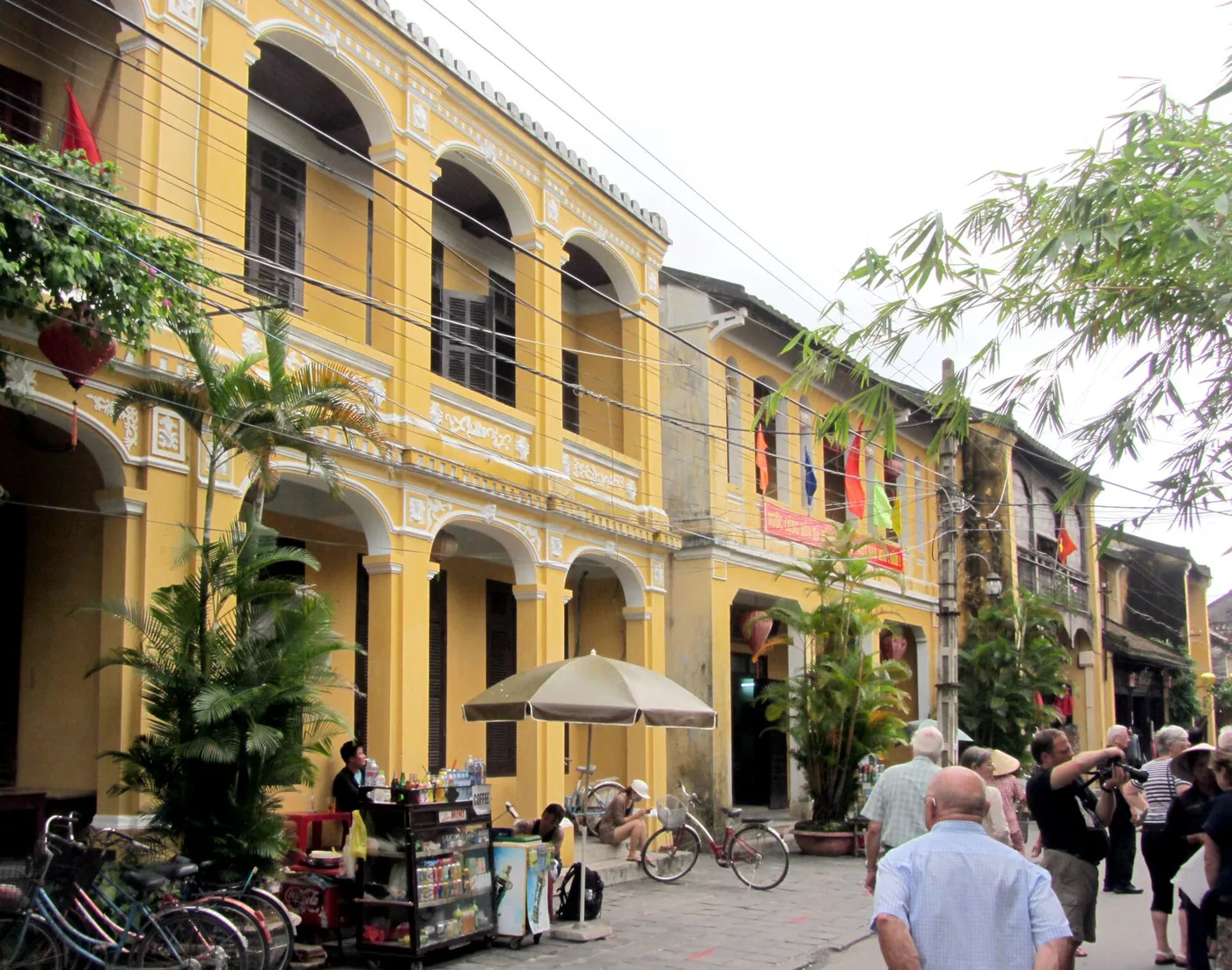 The yellow shophouses along Nguyen Thai Hoc street in Hoi An, arcades at street level and visitors walking past