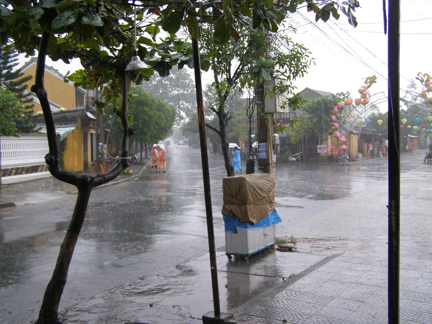 A crossroads in Hoi An during heavy rain, water running across the road and people crossing in raincoats