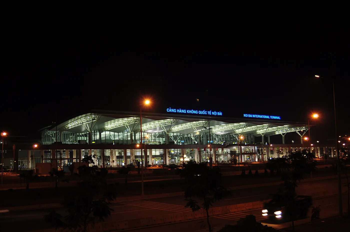 The lit frontage of the international terminal at Noi Bai International Airport, Hanoi, at night, with the airport road running past it
