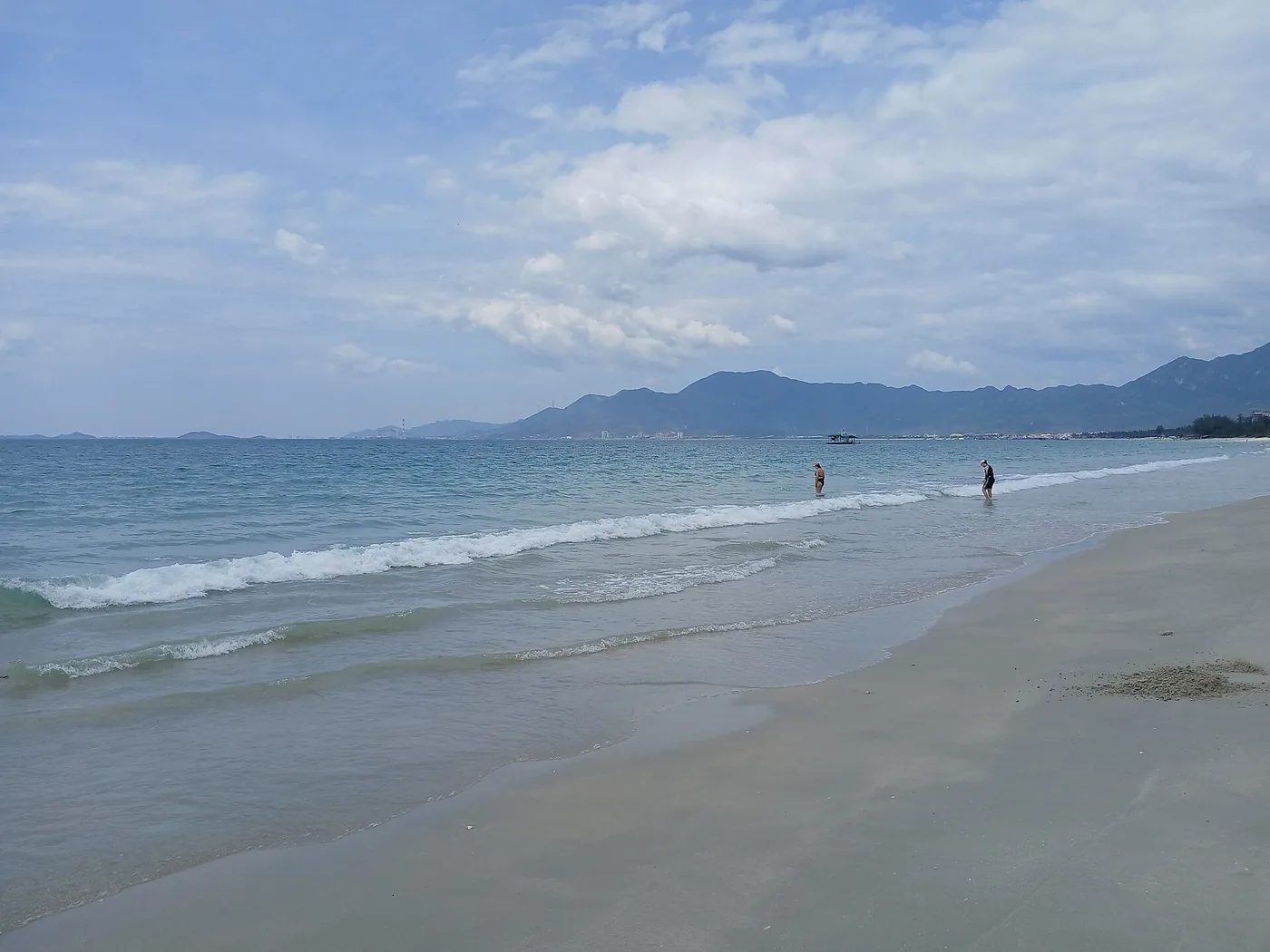 나트랑 북쪽 독렛 해변의 넓은 흰 모래, 얕은 물에 두 사람이 서 있고 수평선에 긴 산줄기