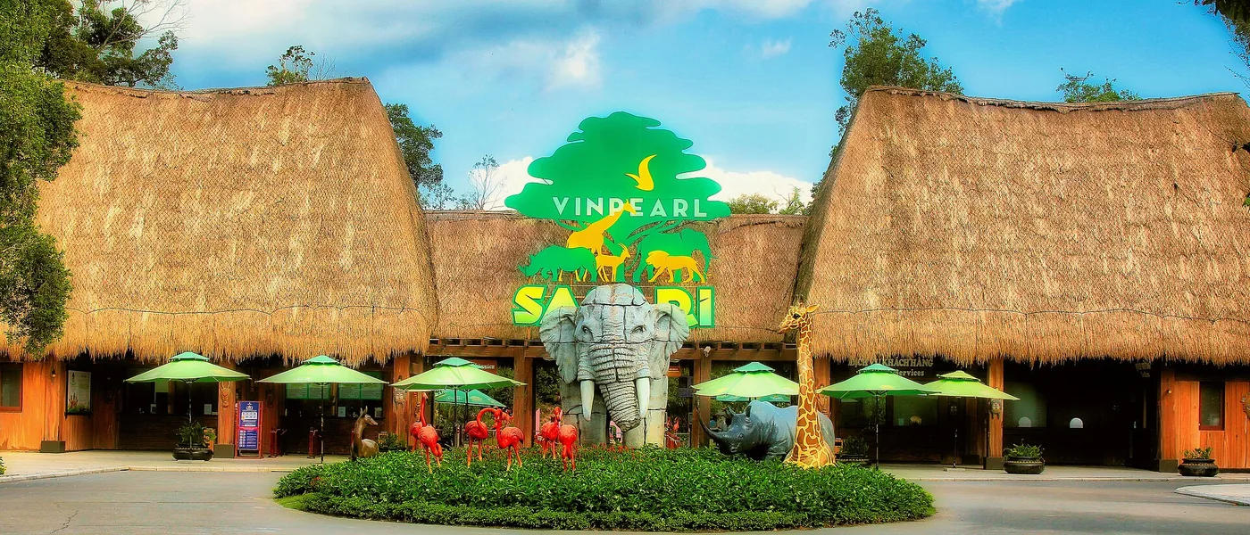 The entrance building of Vinpearl Safari Phu Quoc, with two thatched roofs either side of the safari sign and elephant, giraffe and rhinoceros sculptures in front