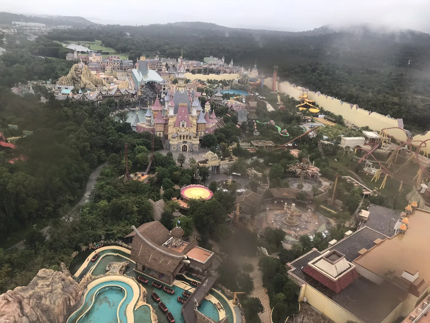 VinWonders Phu Quoc seen from the top of the ferris wheel on an overcast morning, with the central castle, the water park slides on the right and roller coaster track running along the far side