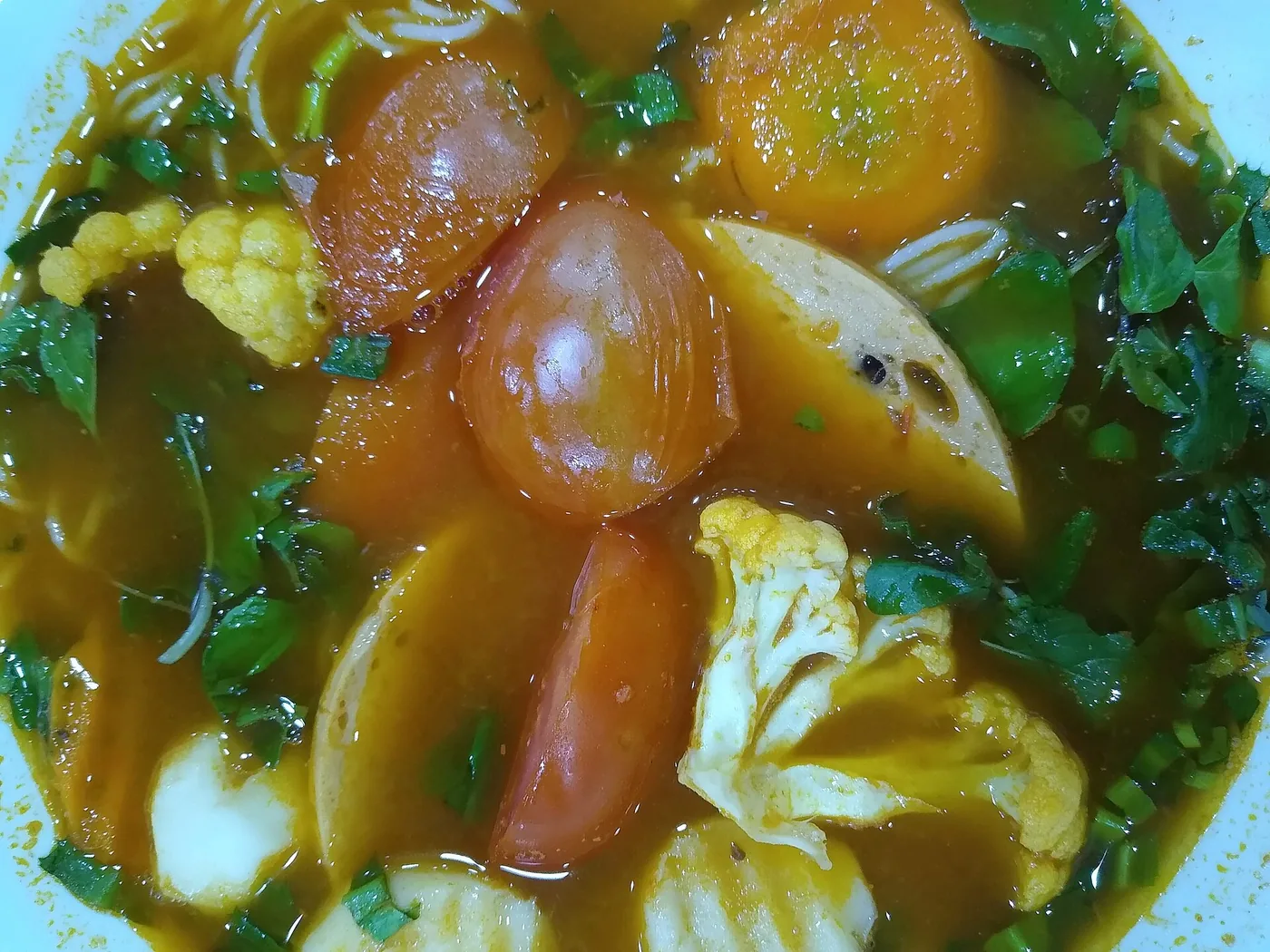 베트남식 채식 국수 한 그릇, 주황빛 국물에 토마토와 콜리플라워, 콩으로 만든 어묵과 허브가 담겨 있다