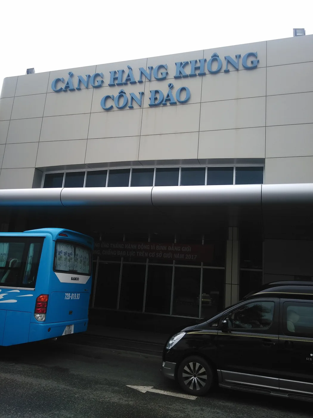 Con Dao airport terminal building with a blue bus and a black car parked outside
