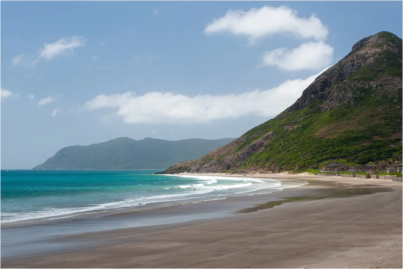 White sand and clear water at Dat Doc beach on Con Dao, with green hills behind
