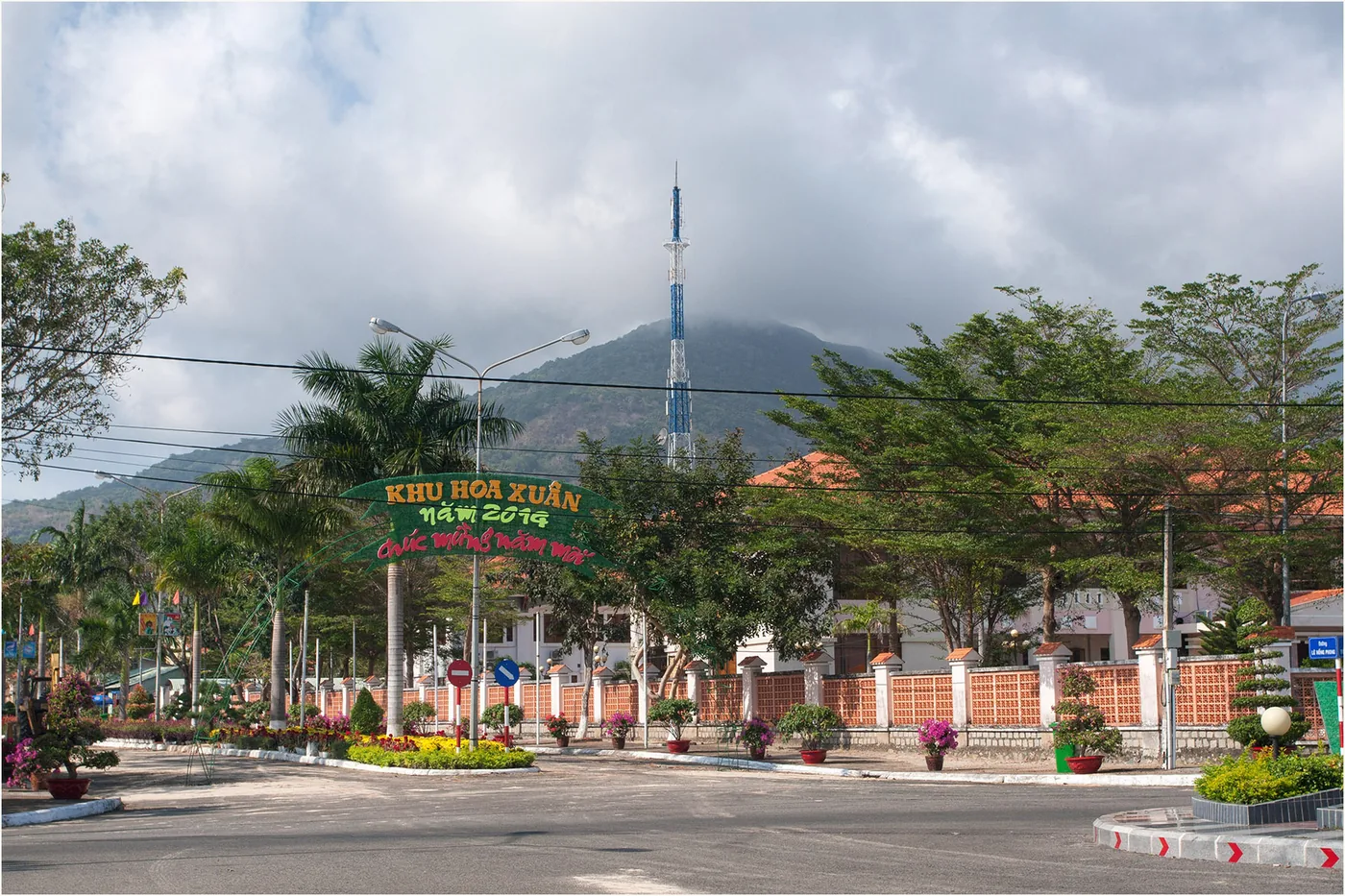A wide street in Con Dao town with flower beds and cloud-covered hills behind