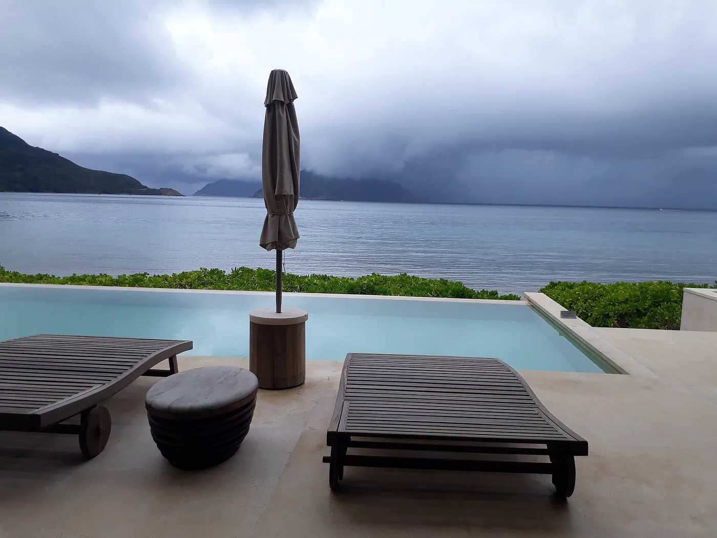 An infinity pool and sun loungers at a Con Dao beach resort, with the sea and green hills beyond