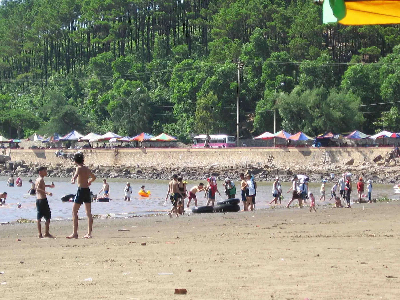 Rows of parasols on Do Son beach with people standing in the shallow water