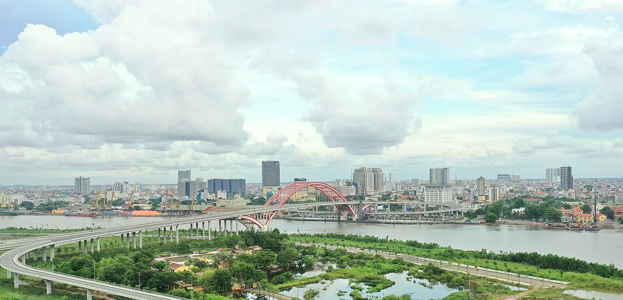 The Hai Phong skyline across a wide river, with a red arch bridge on the left