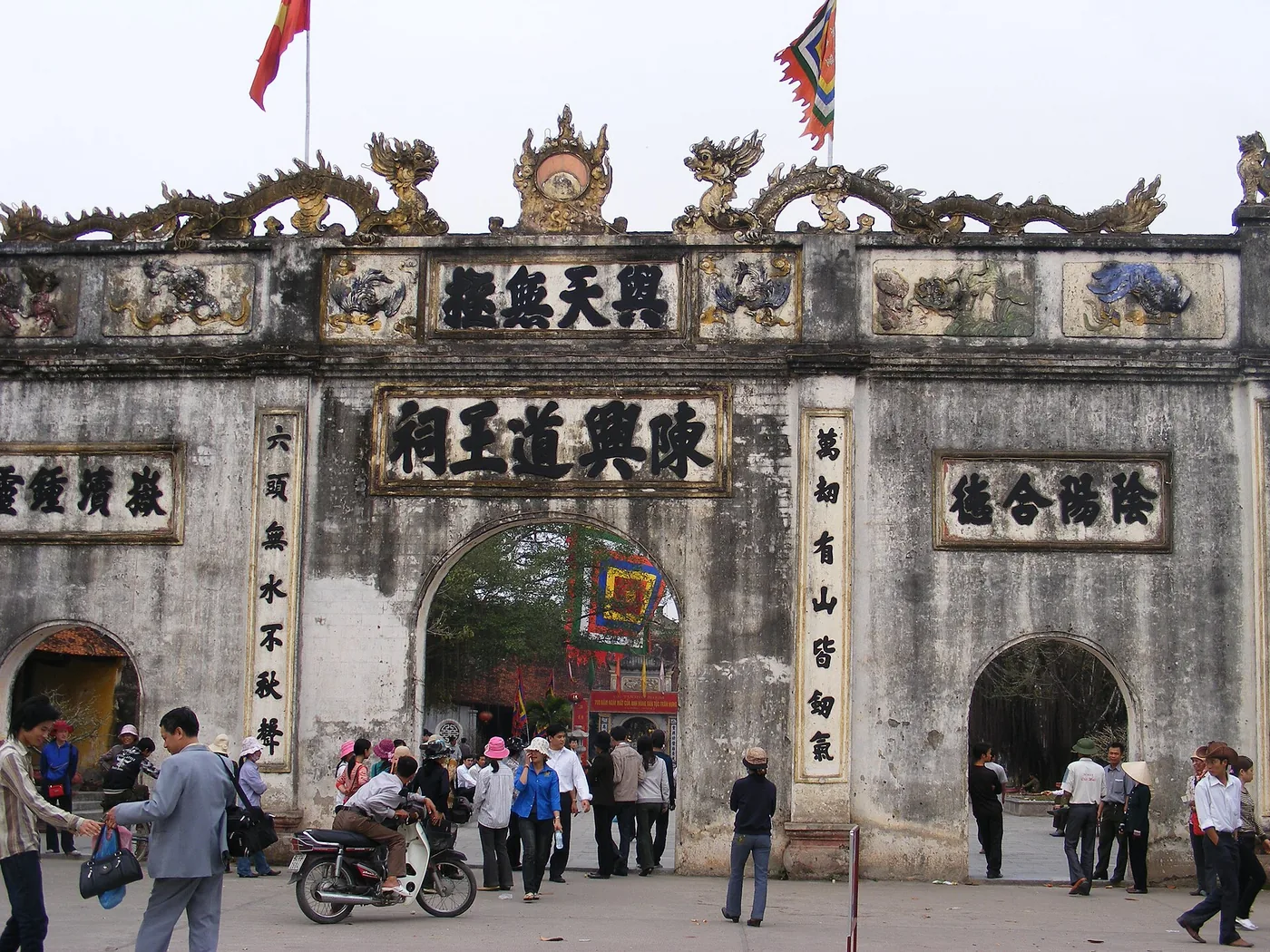The stone triple gate of Kiep Bac temple, hung with Chinese characters, with people walking through