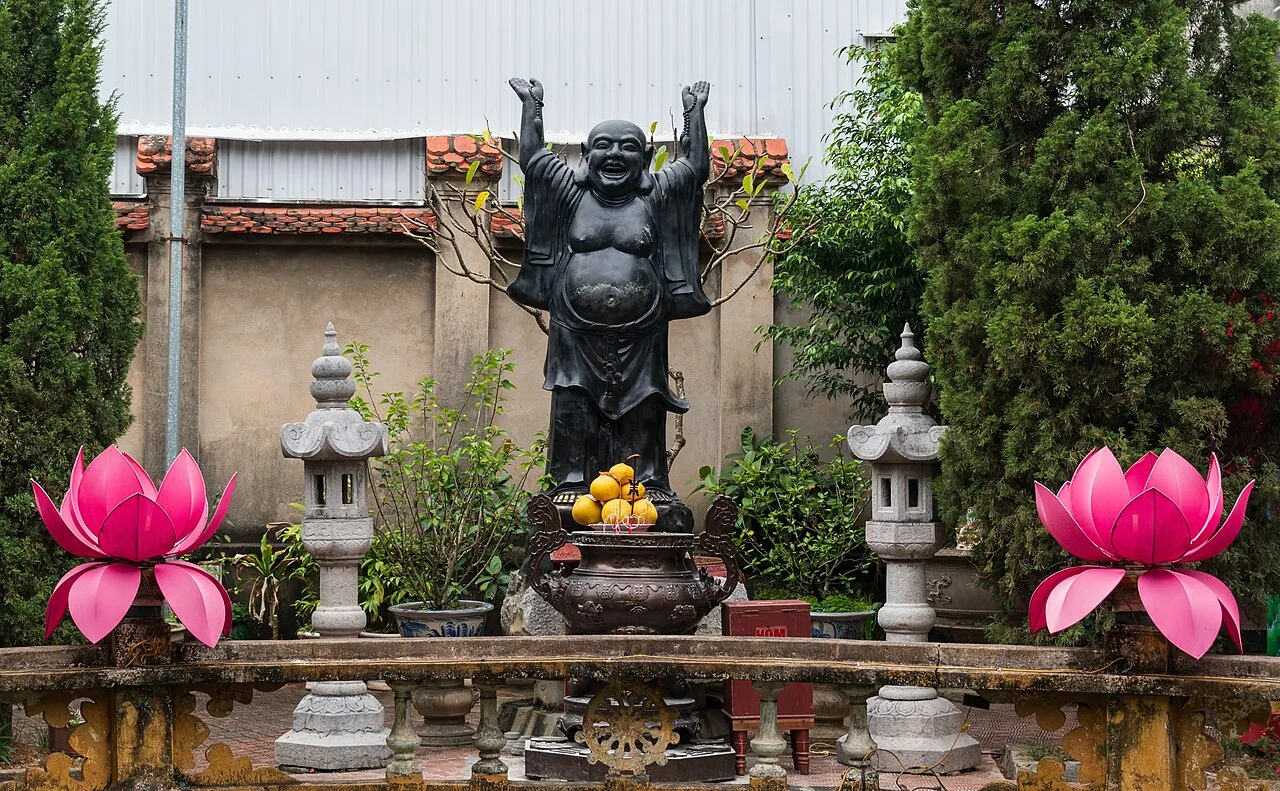 A black Budai statue in the courtyard of Du Hang Pagoda with large pink lotus sculptures on either side