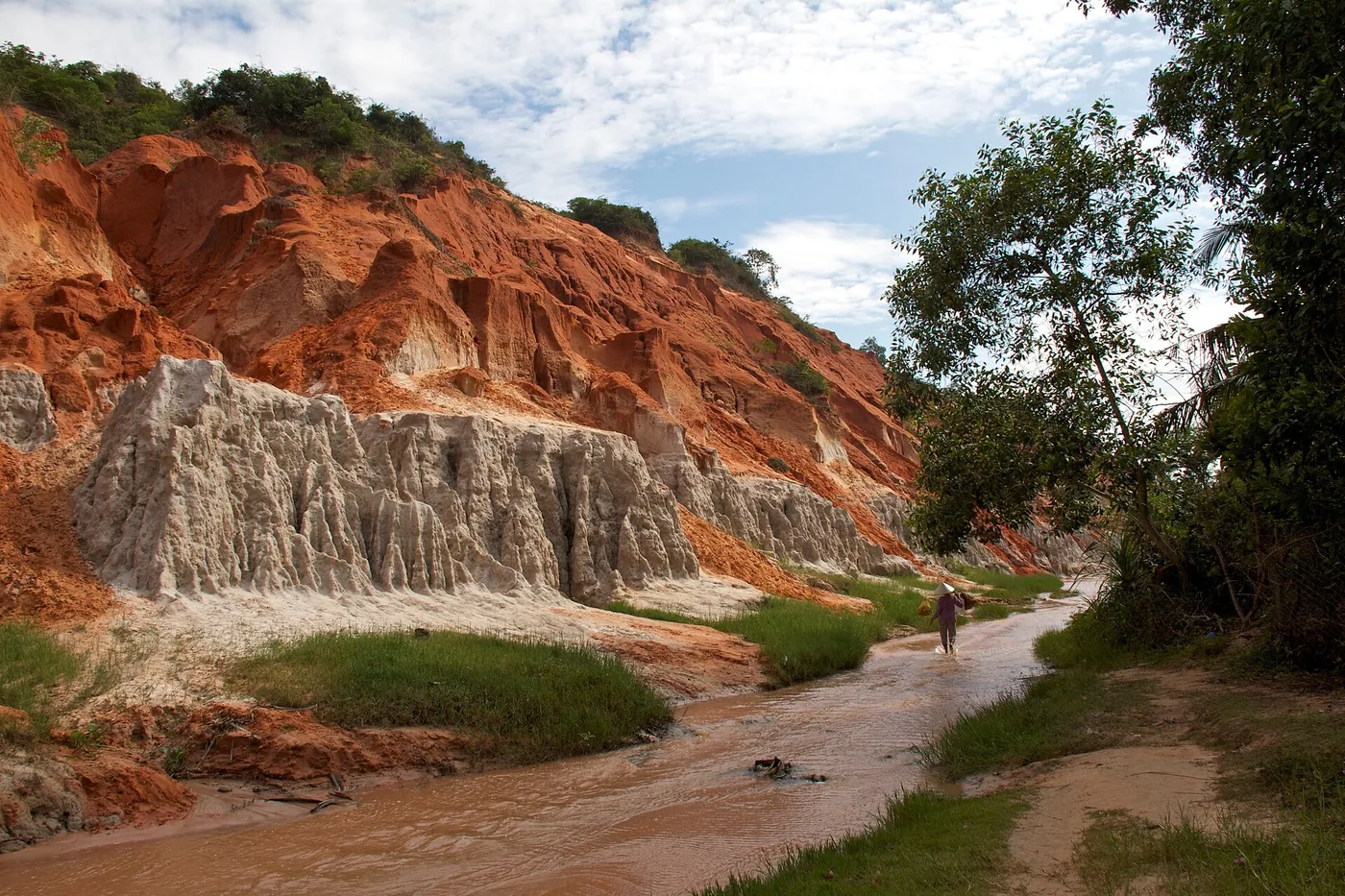 Visitors walking in the shallow water of Fairy Stream between orange and white clay cliffs Visitors walking in the shallow water of Fairy Stream between orange and white clay cliffs